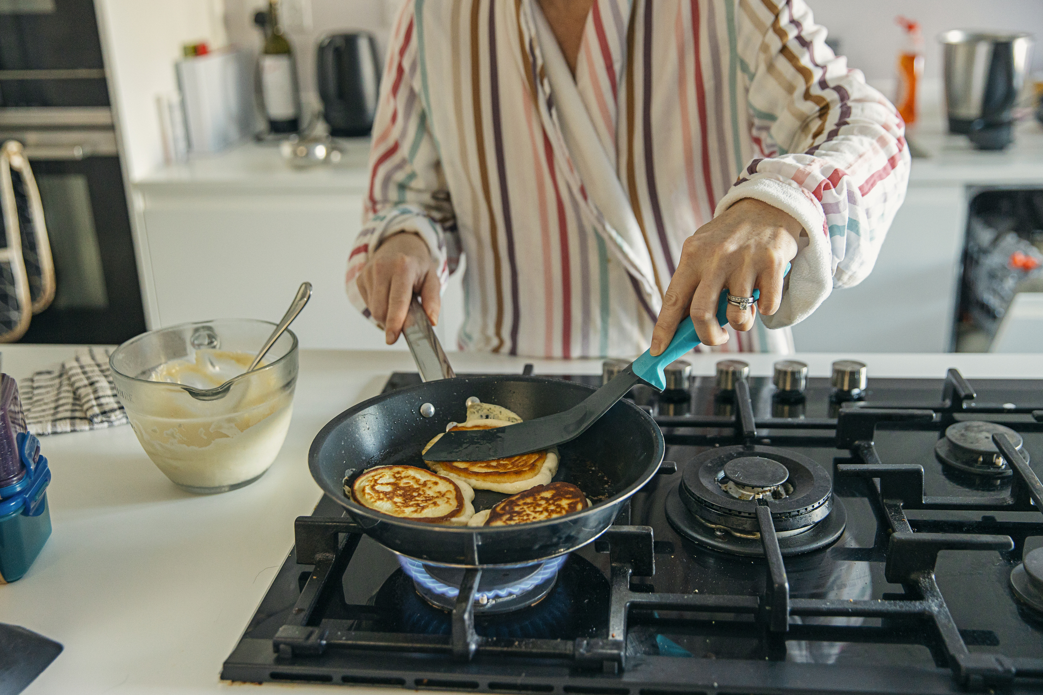 Person cooking pancakes on a stove with a mixing bowl and spoon nearby