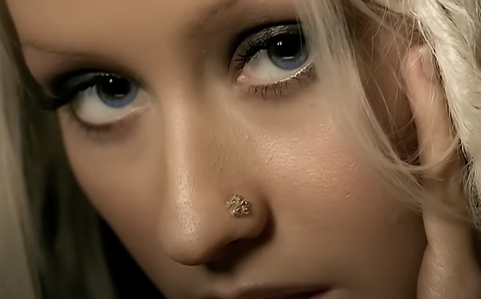 Close-up of Christina Aguilera&#x27;s face with a jeweled nose ring and dramatic eye makeup, looking directly at the camera