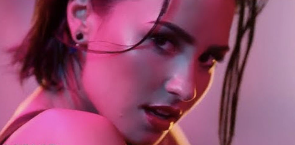 Demi Lovato in a close-up portrait looking over their shoulder with short hair and an intense expression