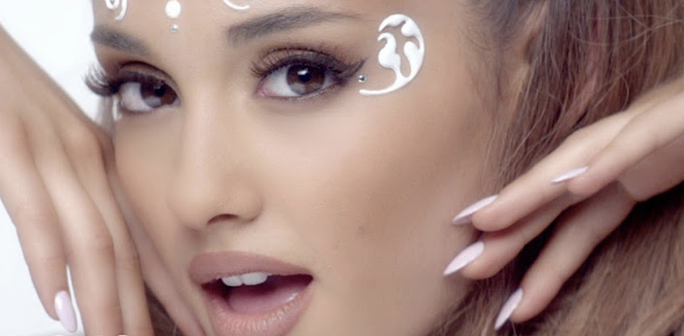 Ariana Grande, with intricate white face paint and manicured nails, poses glamorously