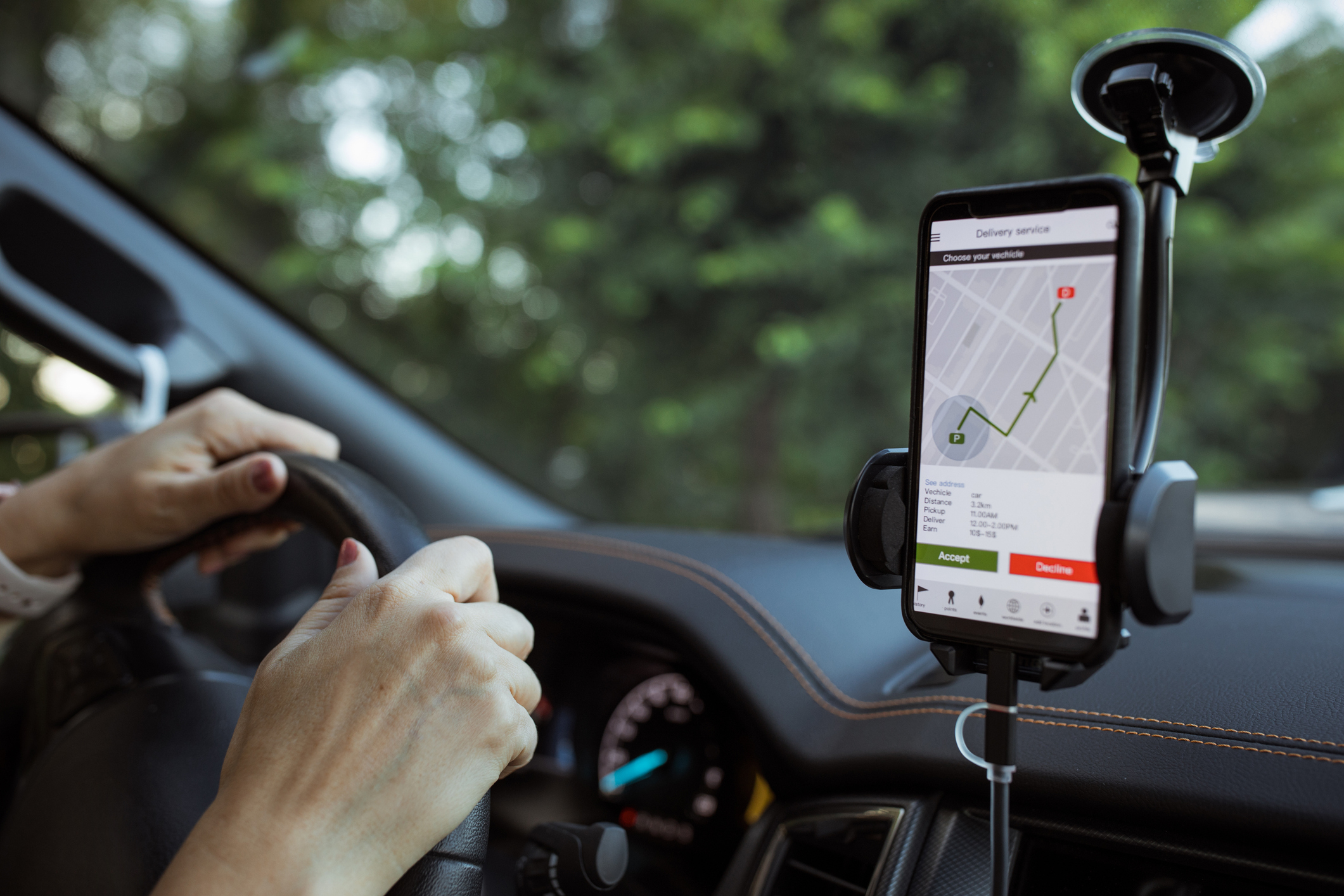 Hands on the steering wheel while a GPS navigation app shows a delivery route on a smartphone mounted in a car