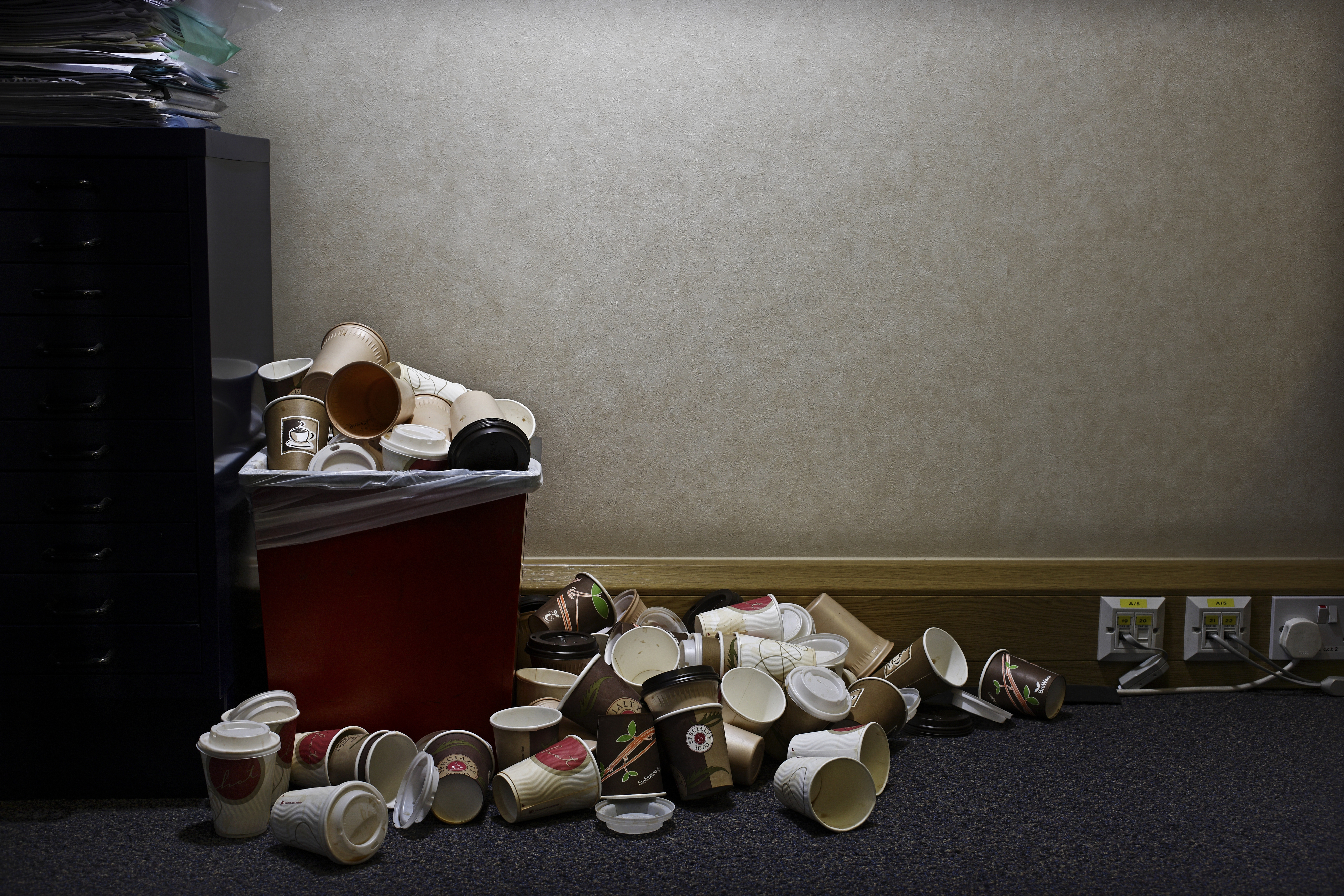 Overflowing trash bin with a pile of discarded coffee cups around it, indicating a high consumption of coffee in the area. No people visible