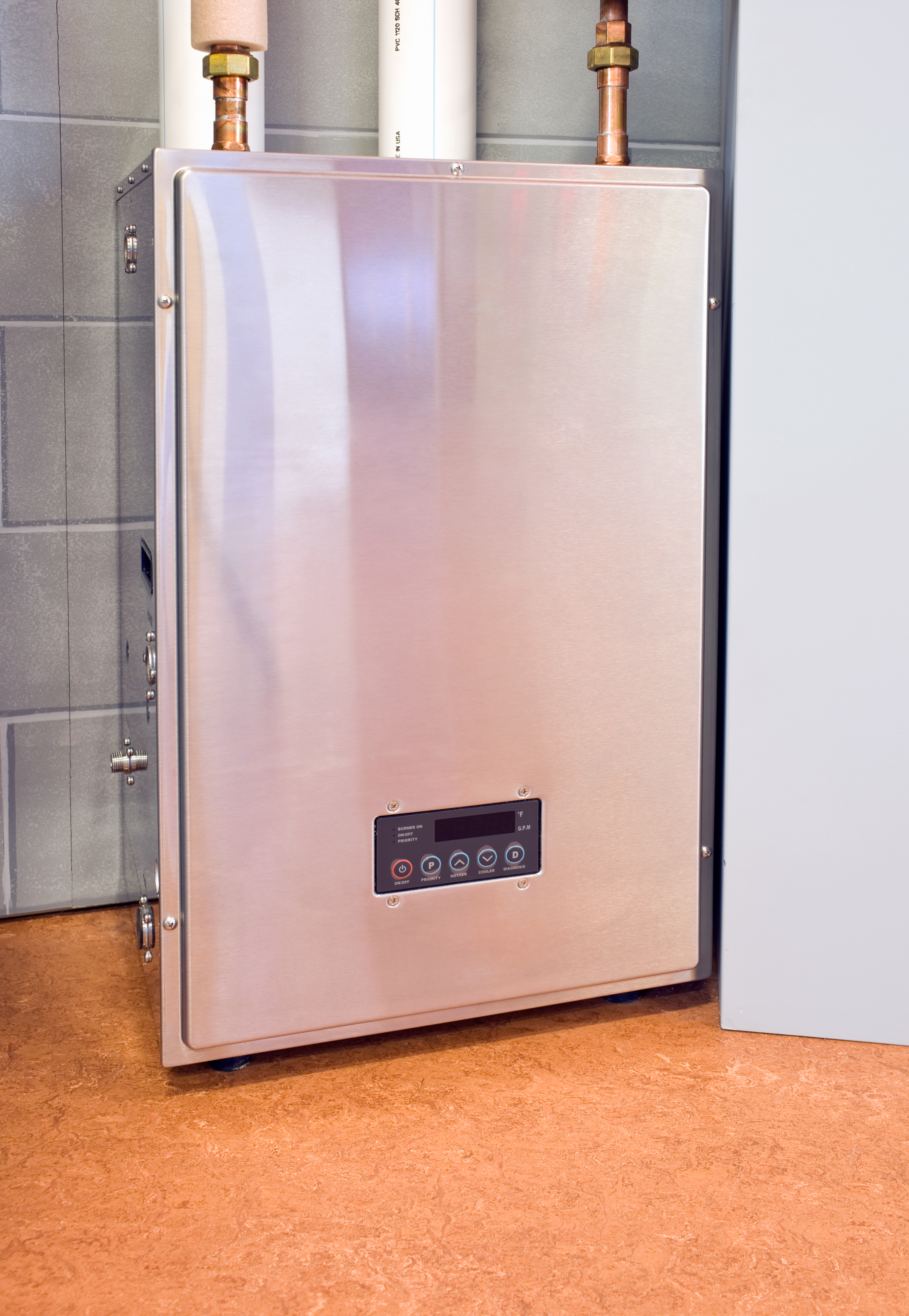 A modern, stainless steel tankless water heater installed on a wall, with pipes connected at the top