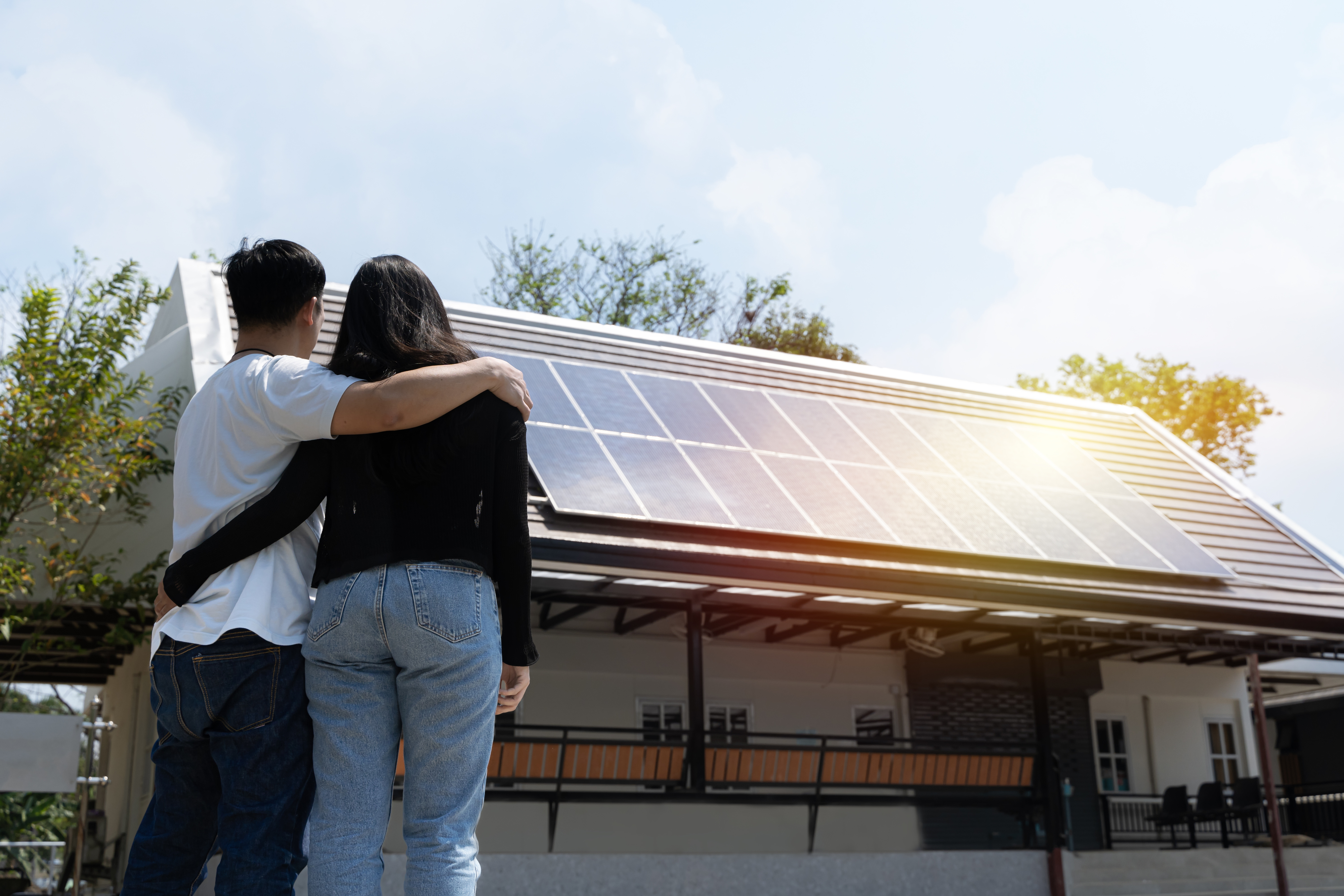 A couple stands with arms around each other, viewing solar panels on a house roof