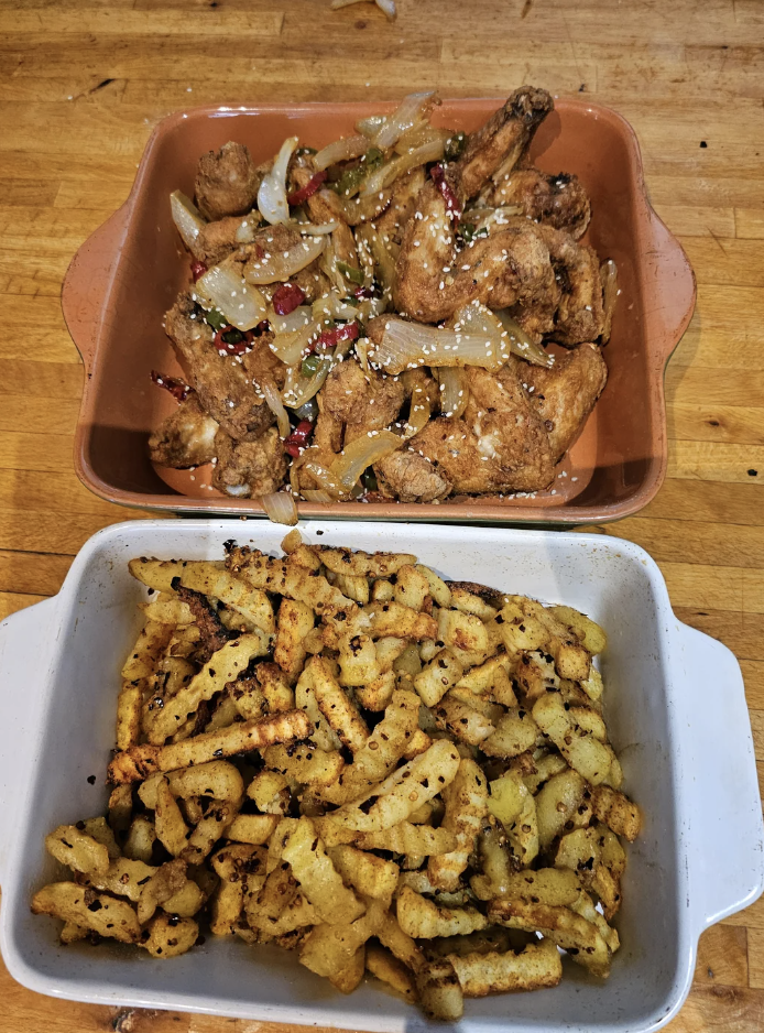 Two baked dishes: one with fried chicken pieces, onions, and peppers in a square tray, and another with seasoned crinkle-cut fries in a rectangular dish