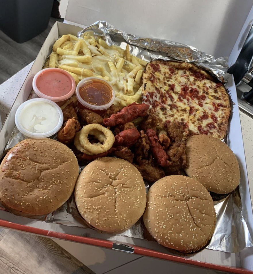 A variety of food items including burgers, fries, pizza, and chicken wings, all packed in an open delivery box