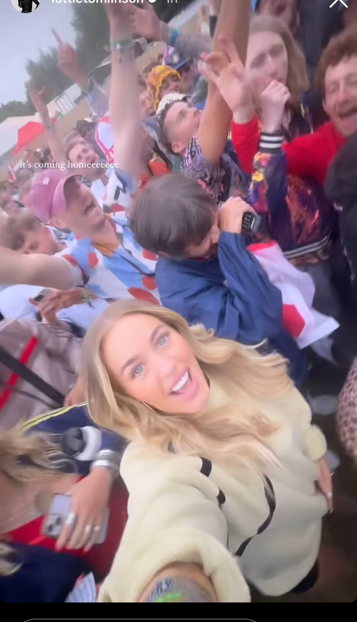 Lottie Tomlinson takes a selfie amidst a cheering crowd of England fans celebrating. She is dressed casually in a light-colored top