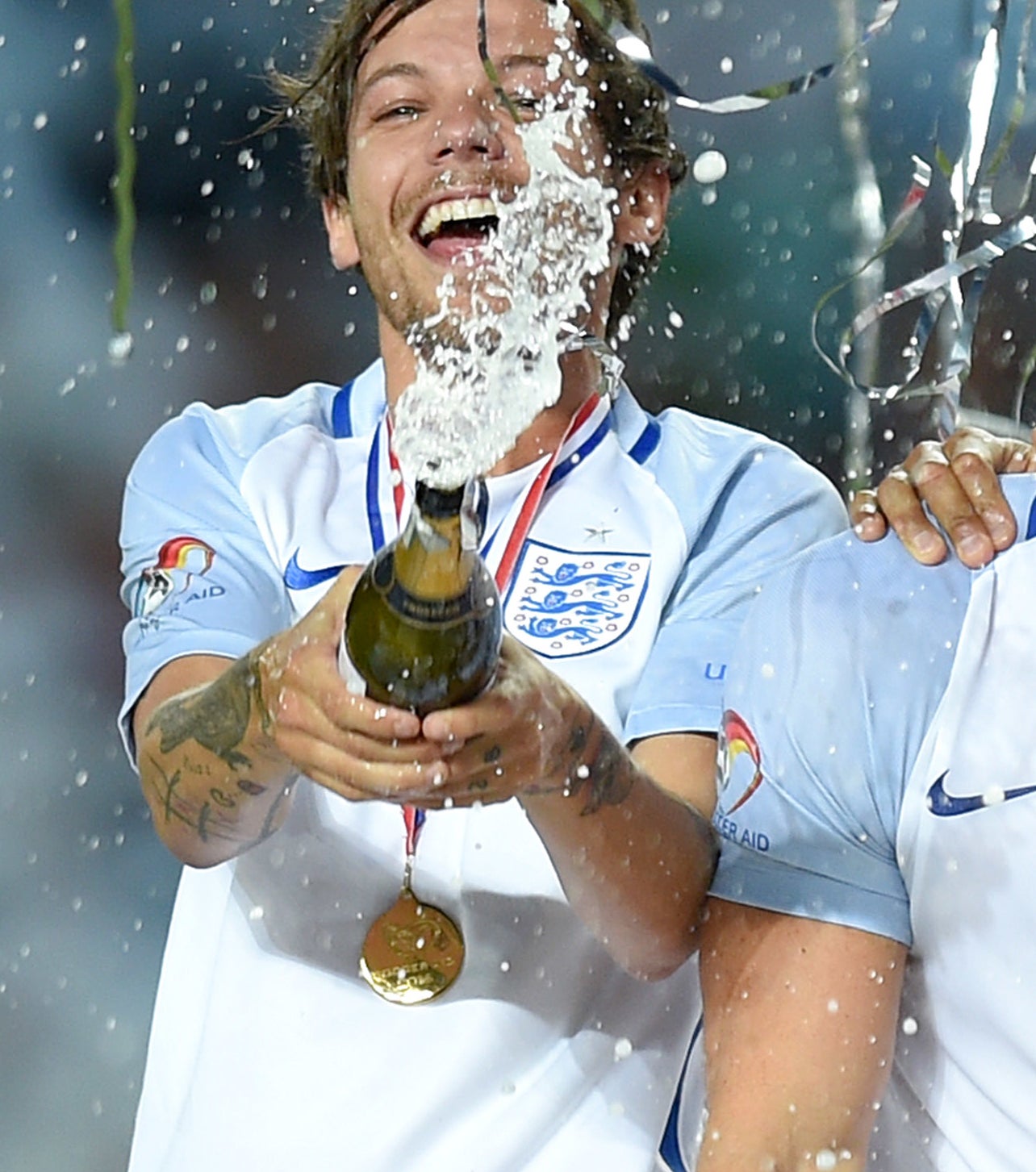 Louis Tomlinson celebratory sprays champagne while wearing a jersey and medal at a sports event