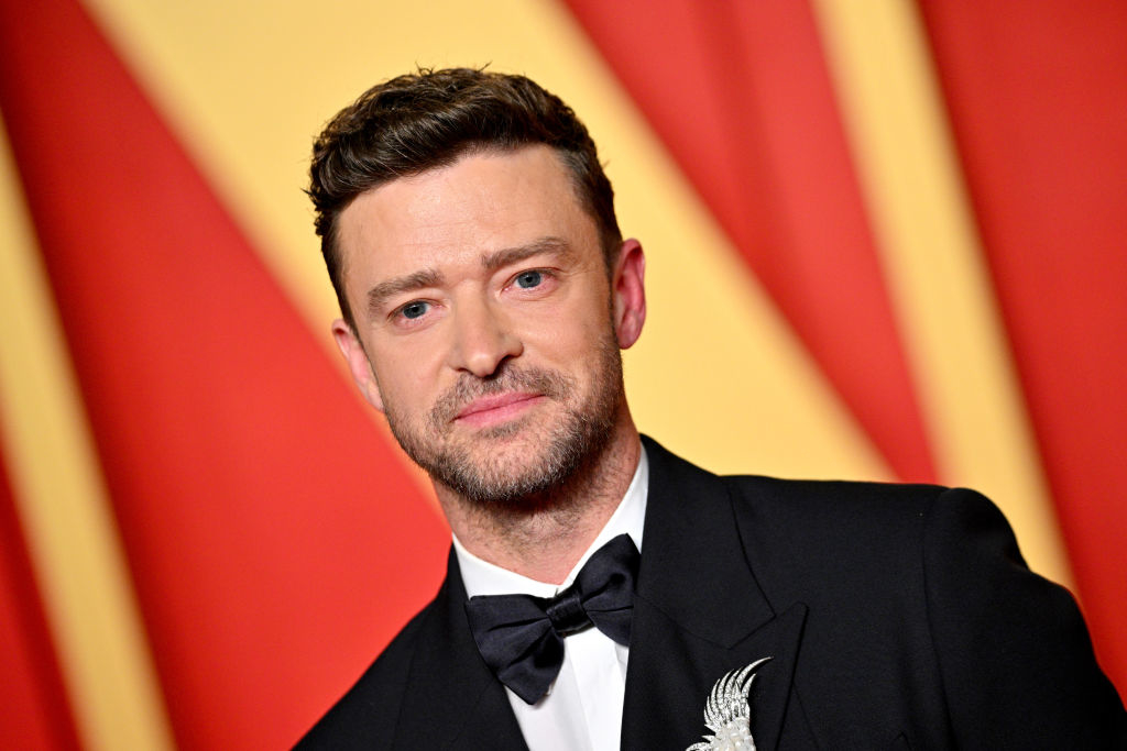 Justin Timberlake in a black suit and bow tie, posing for a photo against a striking backdrop with diagonal lines