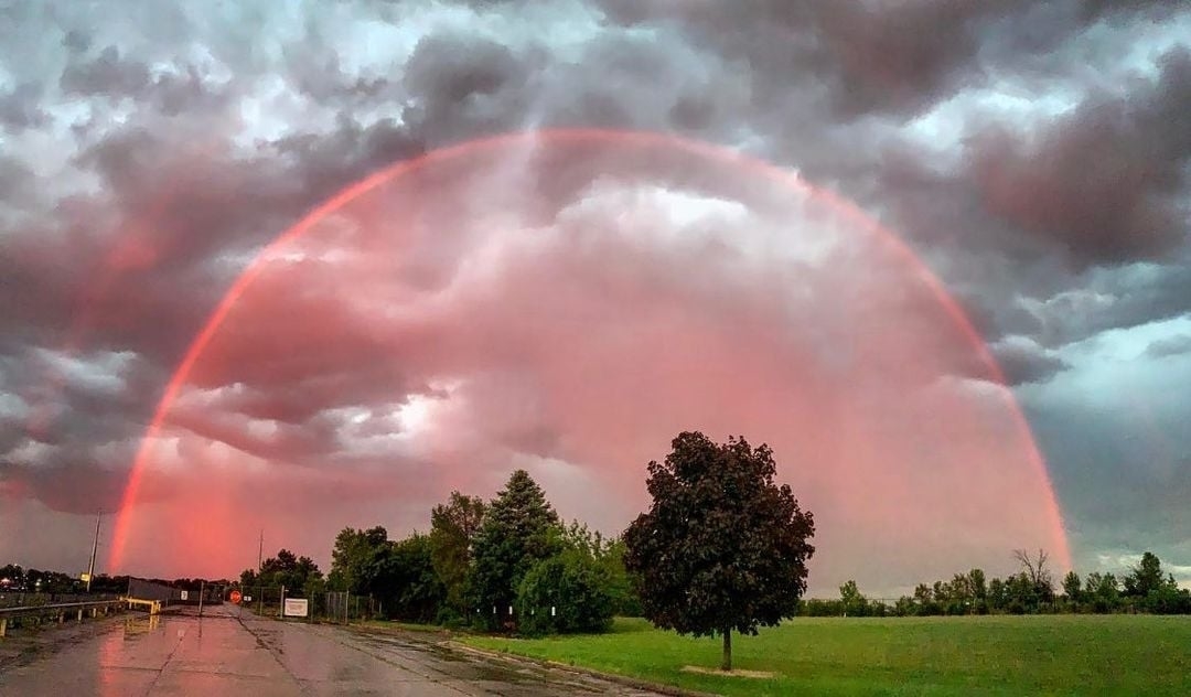 A vibrant red rainbow arches across a ominous sky