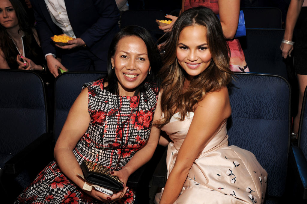 Two women, one in a patterned dress and the other in a strapless gown, smile and sit together in a theater setting