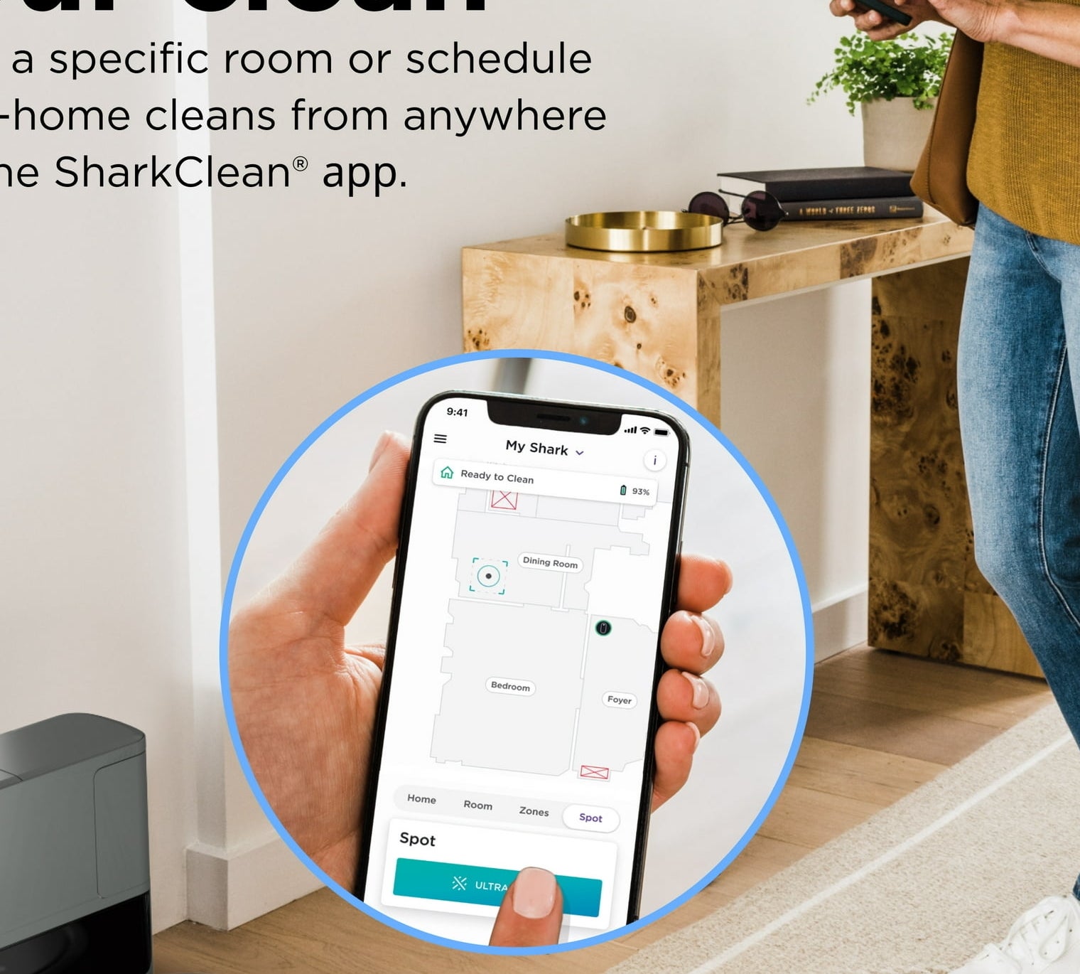 A person using the SharkClean® app on their phone to control a Shark robot vacuum. The app allows room-specific or whole-home cleaning schedules