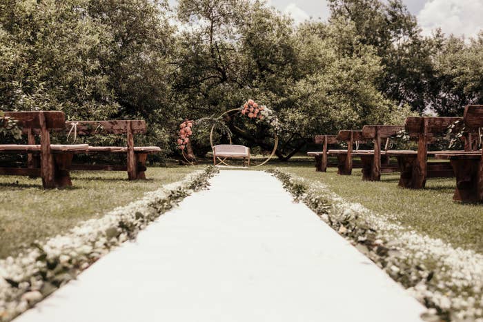 Outdoor wedding ceremony setup with wooden benches and a floral arch at the end of the aisle in a garden setting