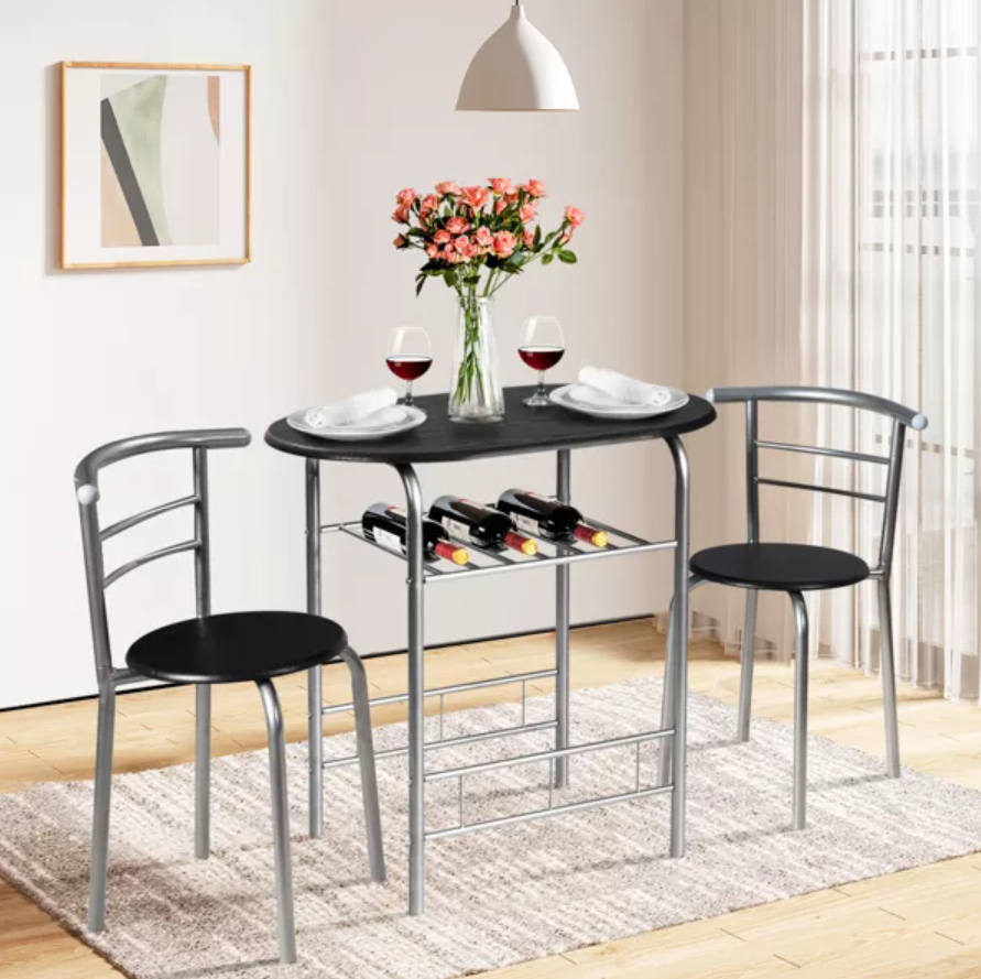 Small dining table set with two chairs, a vase of flowers, two glasses of red wine, and a wine rack underneath.