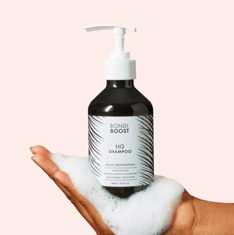 A hand holding a bottle of Bondi Boost HG Shampoo with foam on the palm.