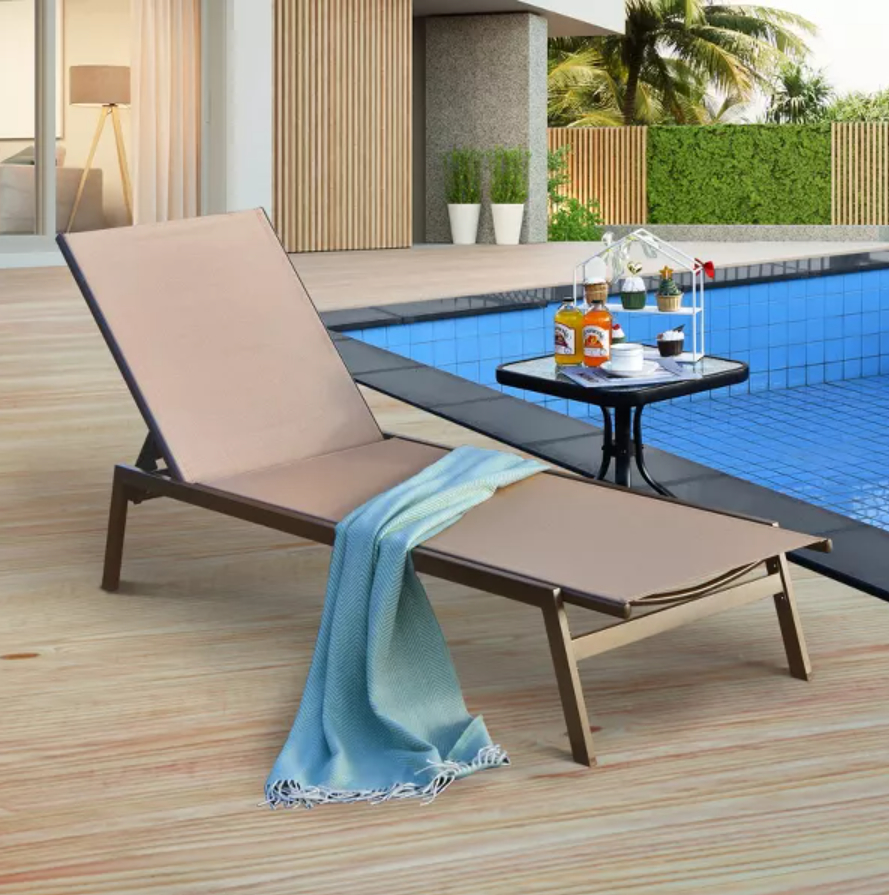 The chaise lounge a nearby table holding a bottle of liquor, a pitcher, and glasses. A blue towel is draped over the chair