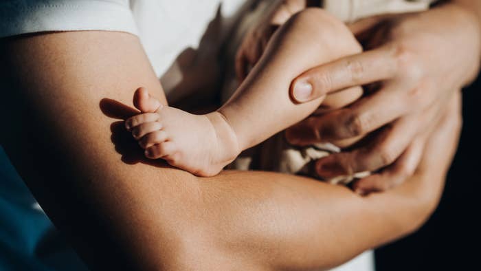 Close-up of an adult holding a baby&#x27;s leg and foot tenderly in their hands, symbolizing parental care and affection