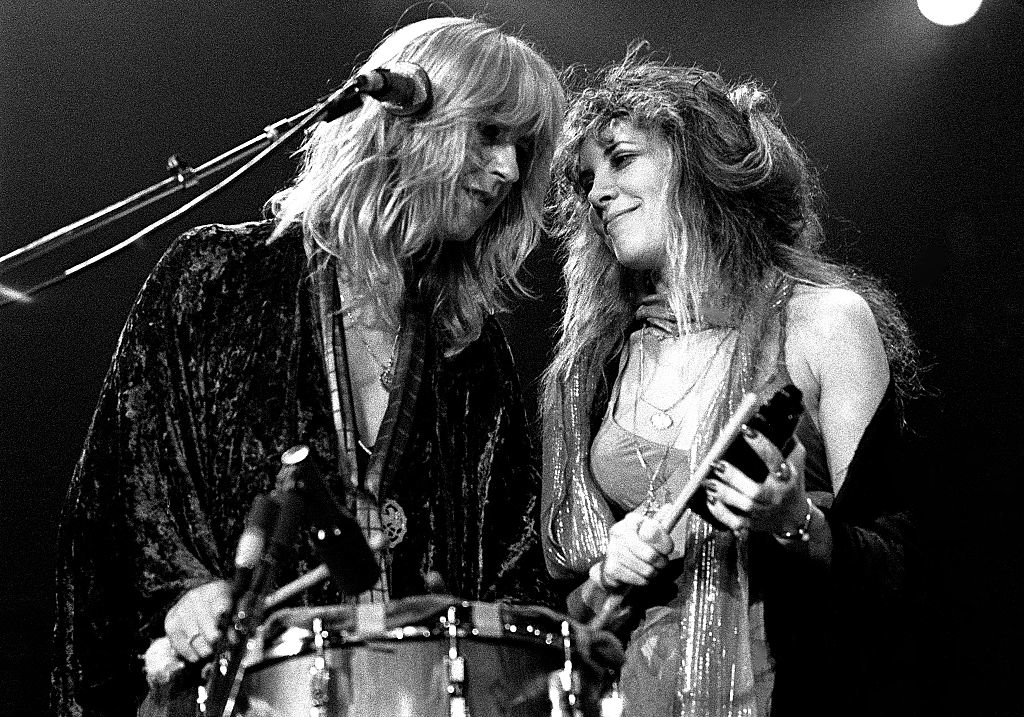 Stevie Nicks and Christine McVie performing on stage, smiling at each other while playing instruments