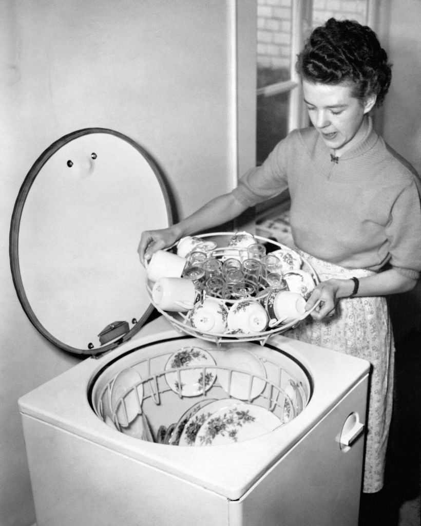 A woman is smiling as she loads dishes into a top-loading dishwasher