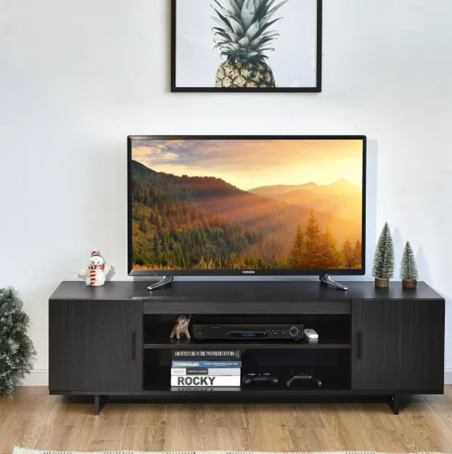 Living room with a wall-mounted TV, a wooden media console with books and decor, two framed artworks, and a potted plant on the left side