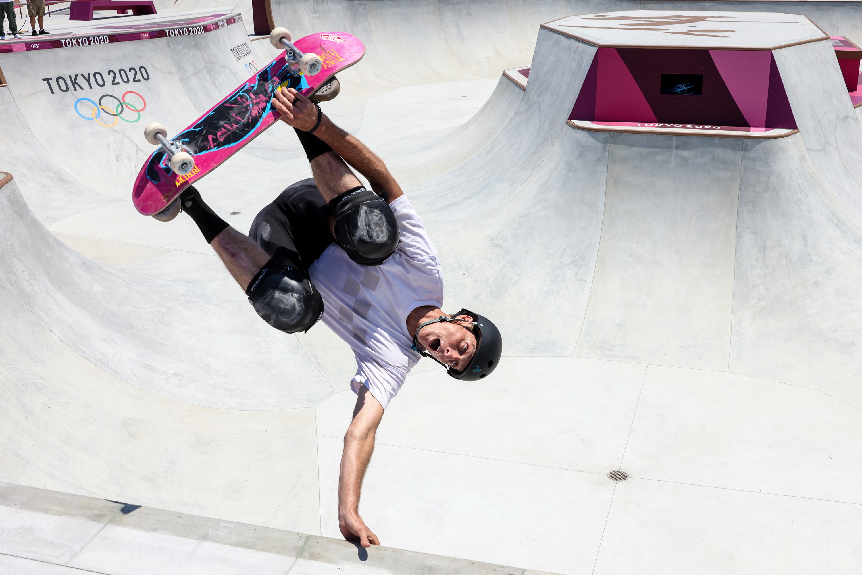 A skateboarder performs a mid-air trick at an Olympic skatepark. &quot;Tokyo 2020&quot; is visible in the background