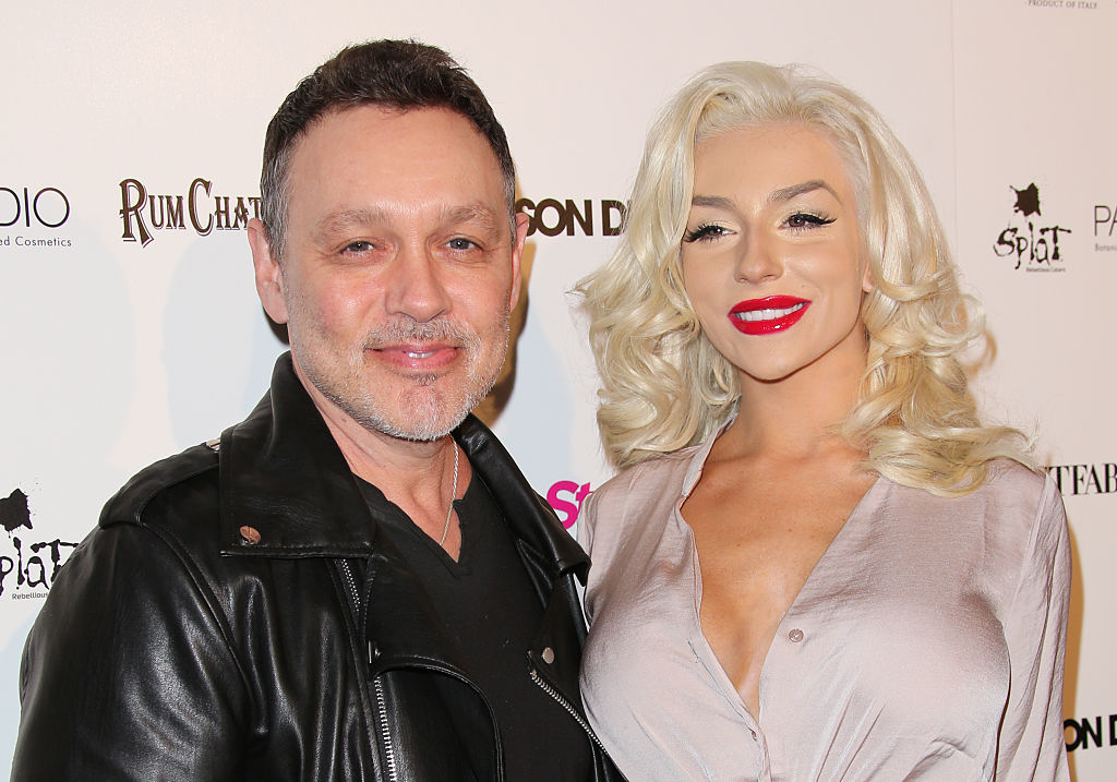 A man in a black leather jacket and a woman in a light blouse, Courtney Stodden, pose together on a red carpet at a Step Up event