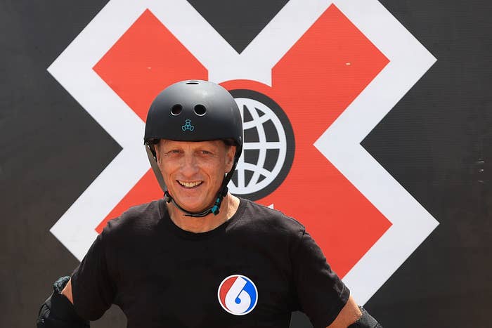Tony Hawk at the X Games, wearing a black helmet and T-shirt with a logo. The background features the X Games symbol