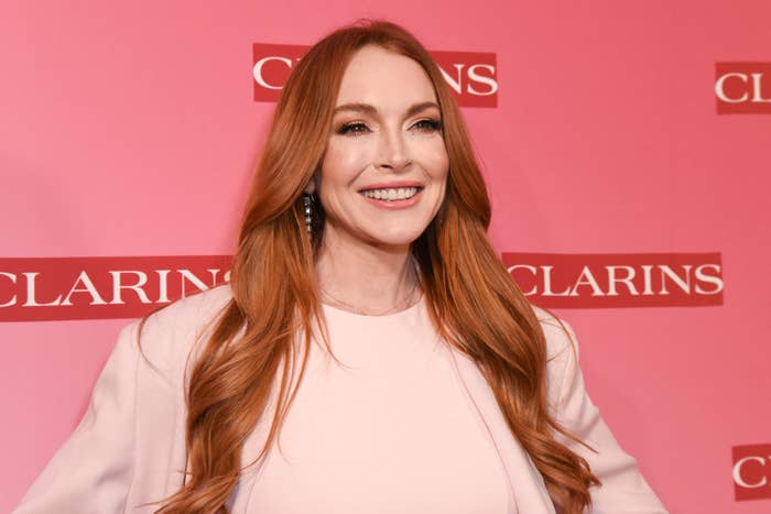 Lindsay Lohan smiling at a Clarins event, with long, wavy hair and dressed in a simple, elegant outfit