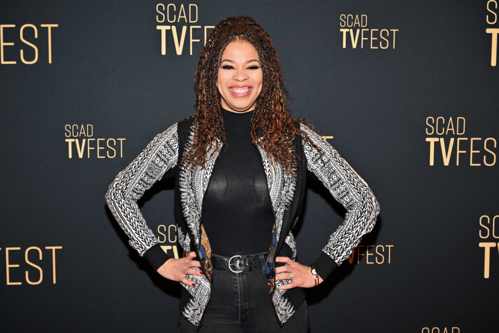 Nkechi in a black-and-white patterned jacket and black pants smiling at SCAD TVFest event backdrop