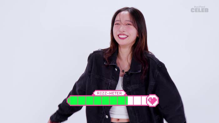 Hannah Bahng standing and smiling. She is wearing a casual black jacket over a white crop top. A graphic labeled &quot;Rizz-Meter&quot; appears with a love heart symbol