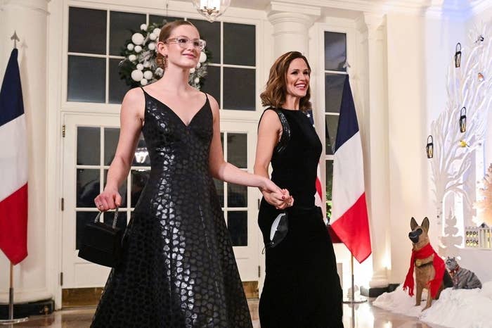 Jennifer Garner and her daughter, Violet Affleck, are holding hands while wearing elegant evening gowns at a formal event with French flags in the background