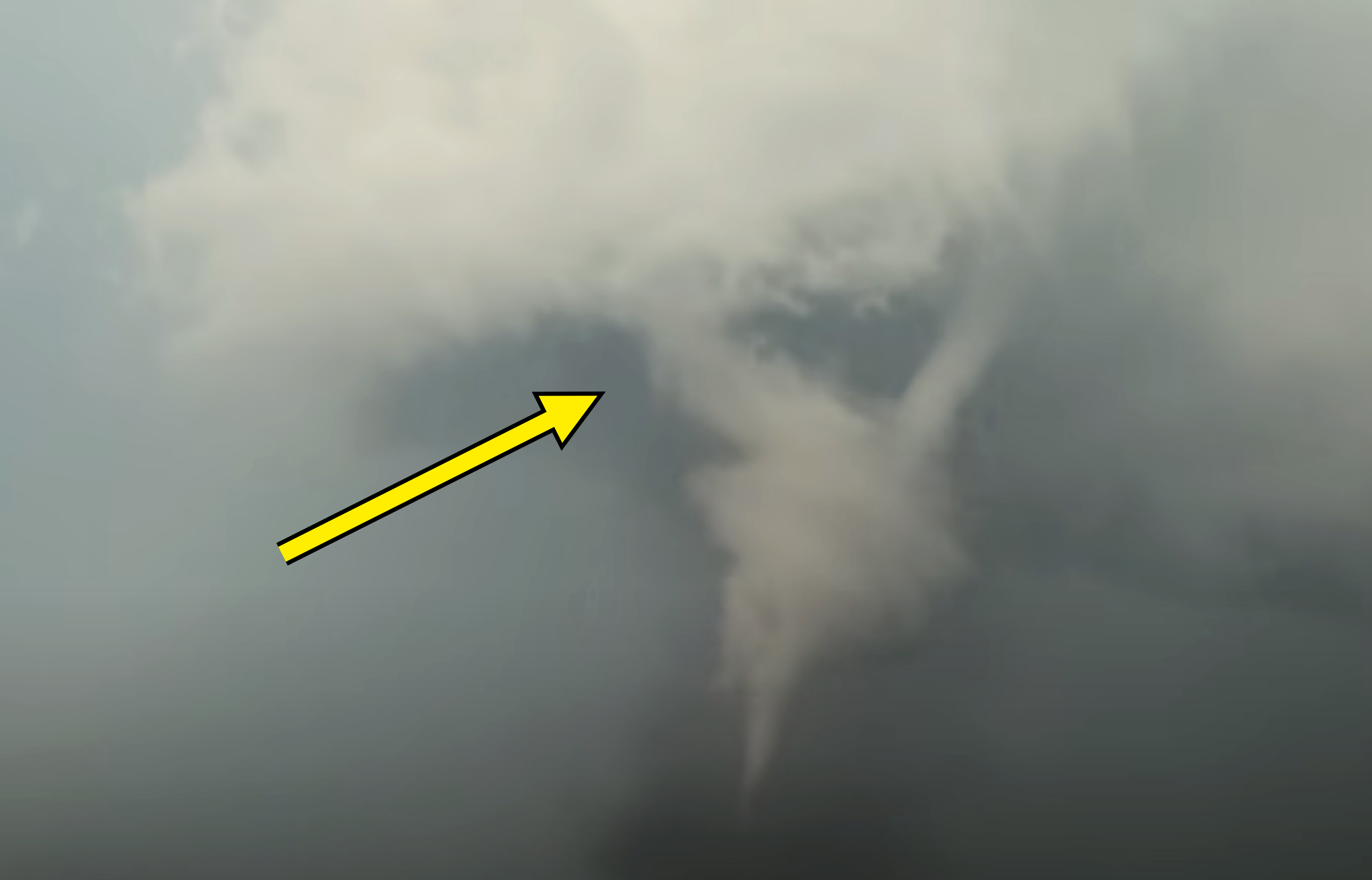 A tornado descends from a large, swirling mass of clouds in the sky, forming a funnel as it touches the ground