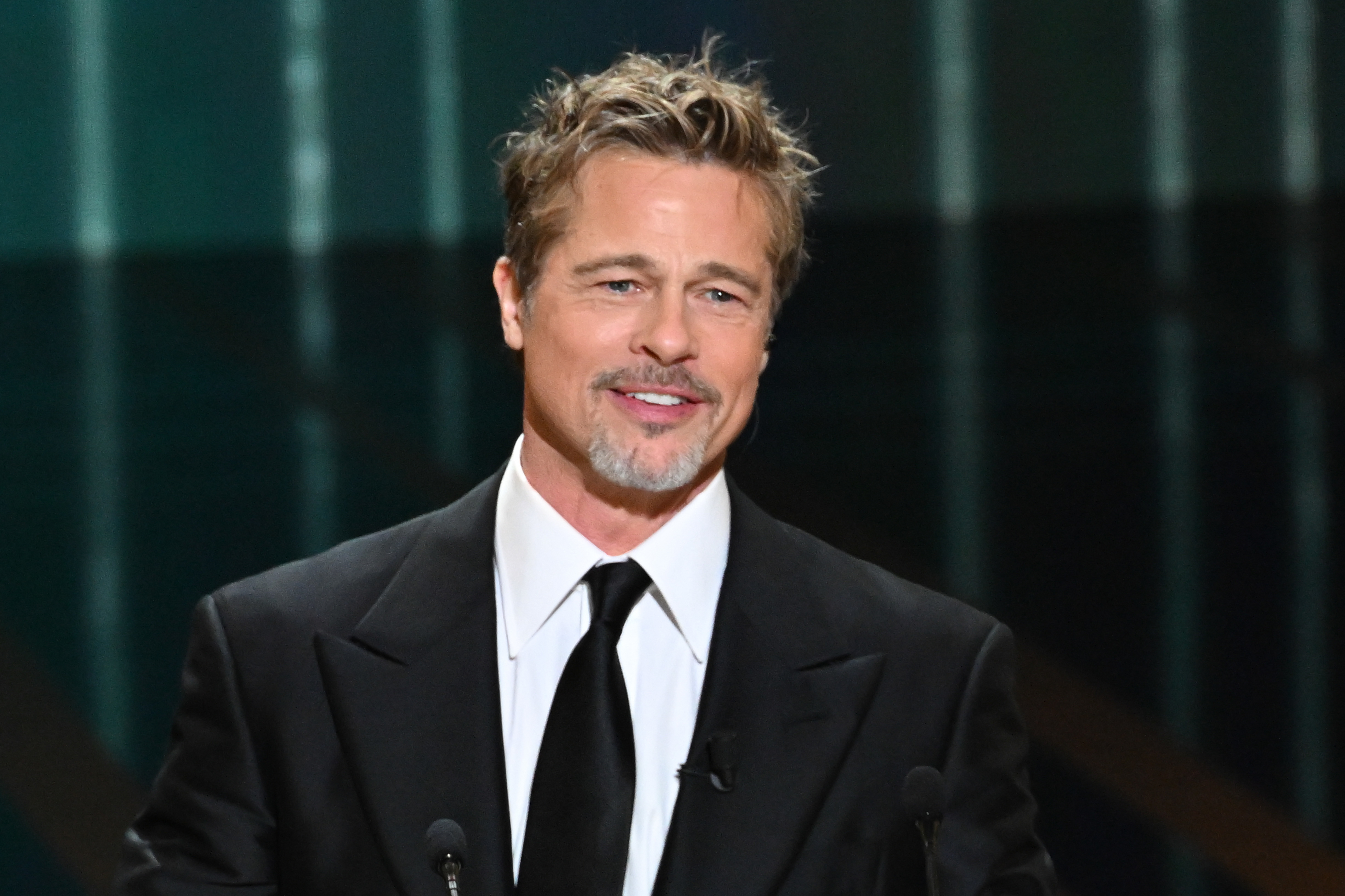 Brad Pitt smiling, wearing a black suit and black tie