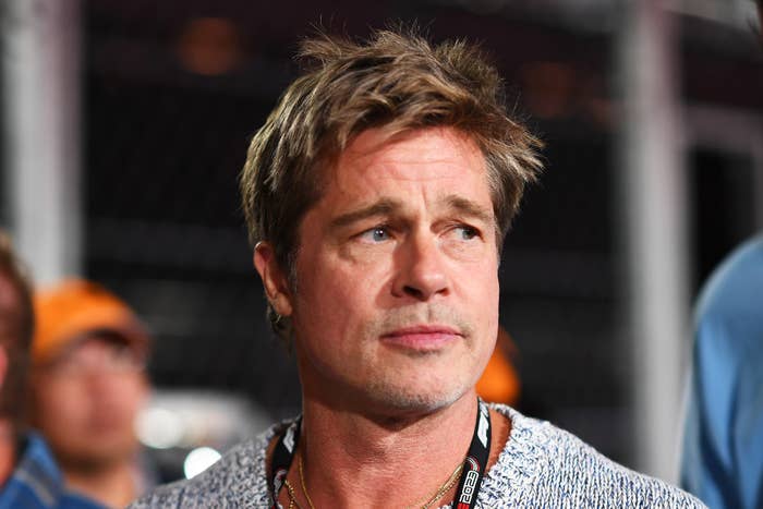 Brad Pitt at a public event wearing a casual sweater with a lanyard around his neck