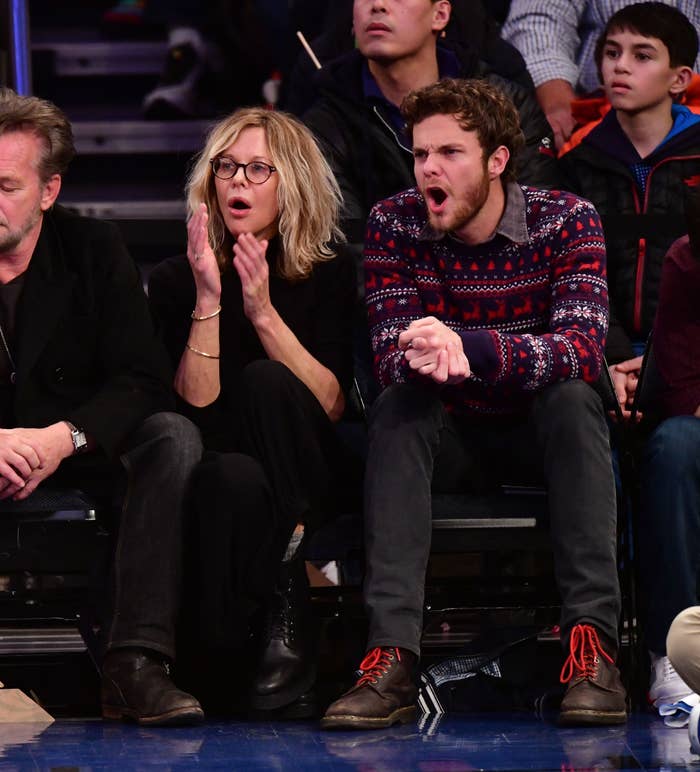 Meg Ryan and Jack Quaid are sitting courtside at a basketball game, reacting to the action on the court. Meg is clapping, and Adam is yawning