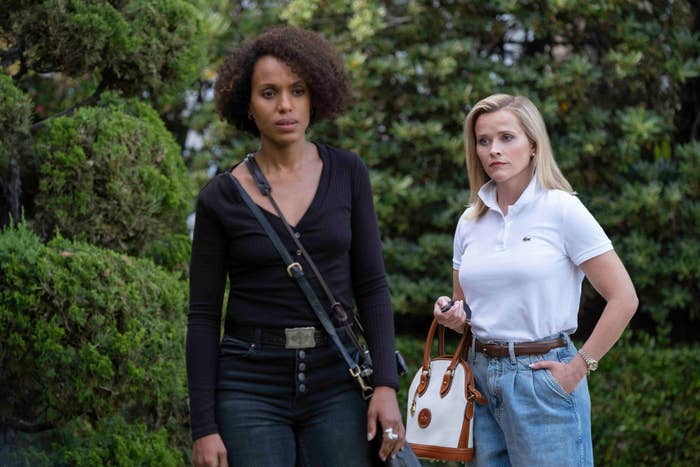 Kerry Washington in a black V-neck top and jeans, and Reese Witherspoon in a white polo shirt and blue high-waisted jeans, standing outdoors