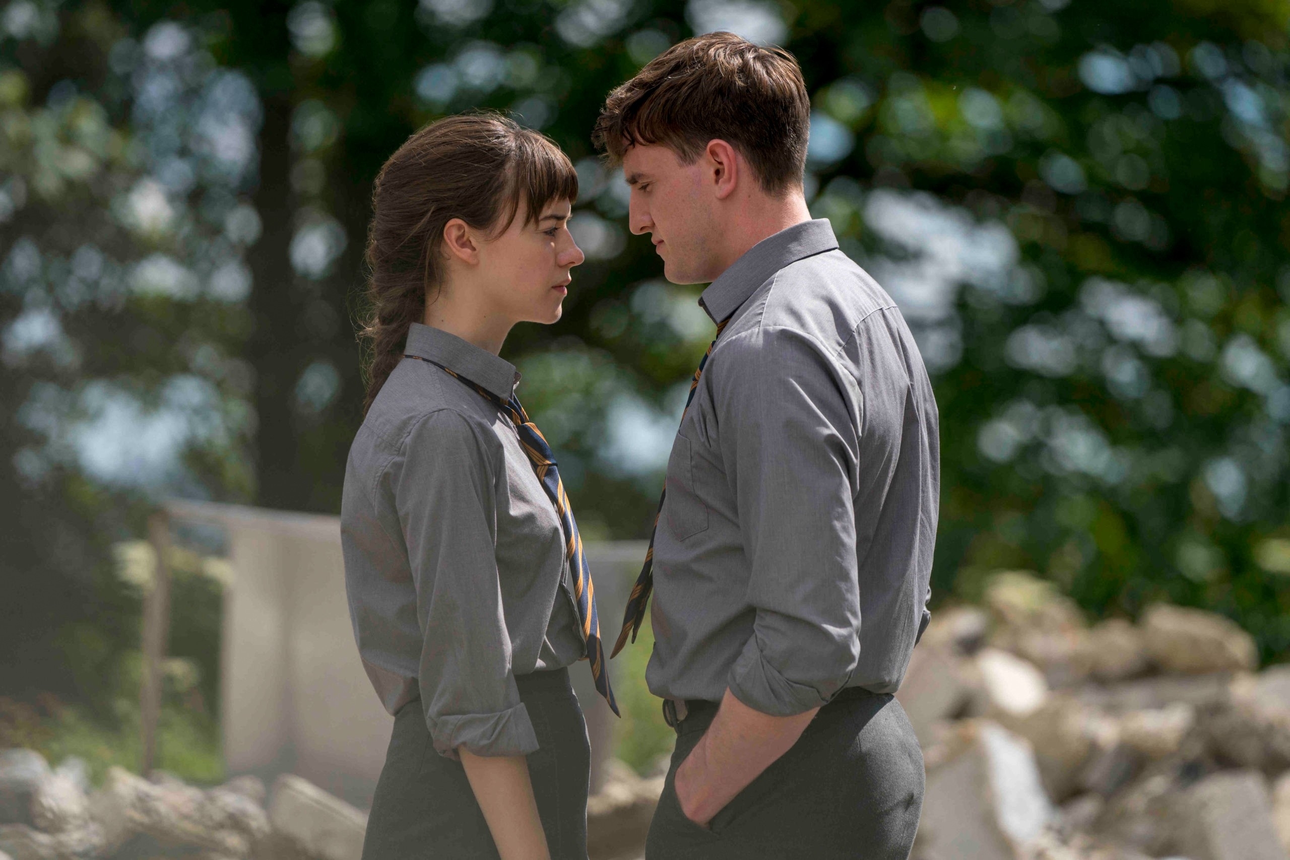 Daisy Edgar-Jones and Paul Mescal stand close, face-to-face, wearing school uniforms in an outdoor setting