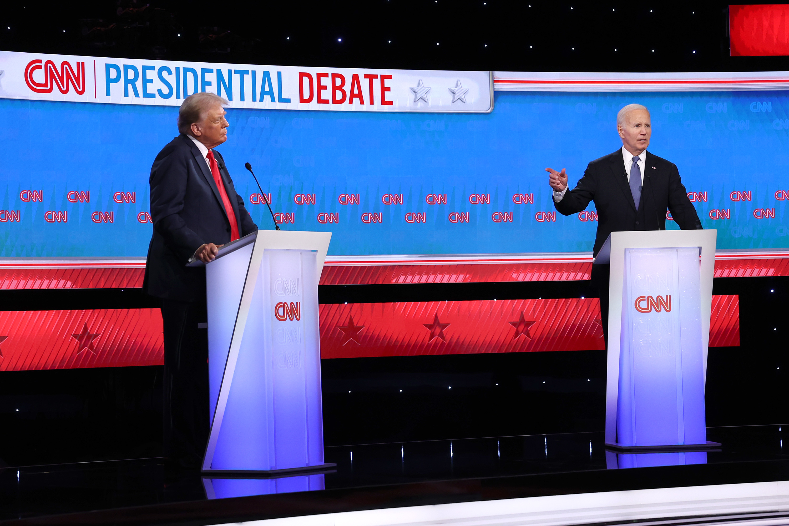 Donald Trump and Joe Biden stand at podiums on a stage during a CNN Presidential Debate. Trump gestures, while Biden speaks