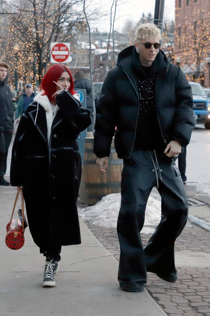 Megan Fox and Machine Gun Kelly walk hand-in-hand on a snowy street, both dressed in stylish, oversized winter clothing