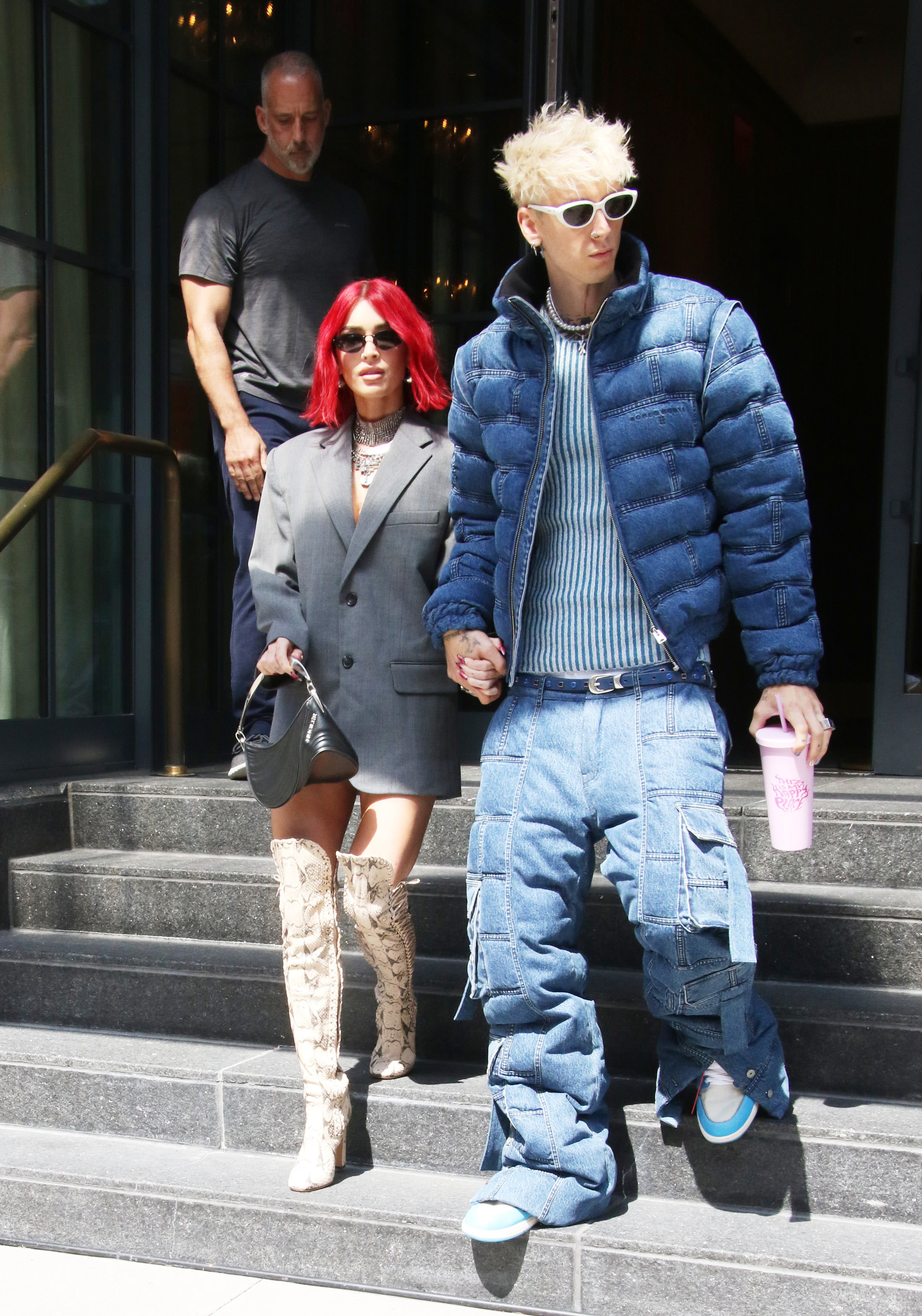 Megan Fox and Machine Gun Kelly step out holding hands; Megan wears a tailored blazer and knee-high boots, while MGK sports a puffer jacket and baggy jeans