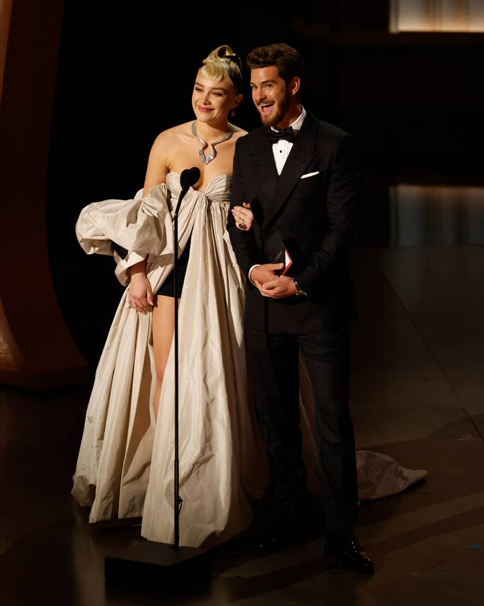 Florence Pugh in a high-slit gown and Andrew Garfield in a tuxedo speak at an awards ceremony