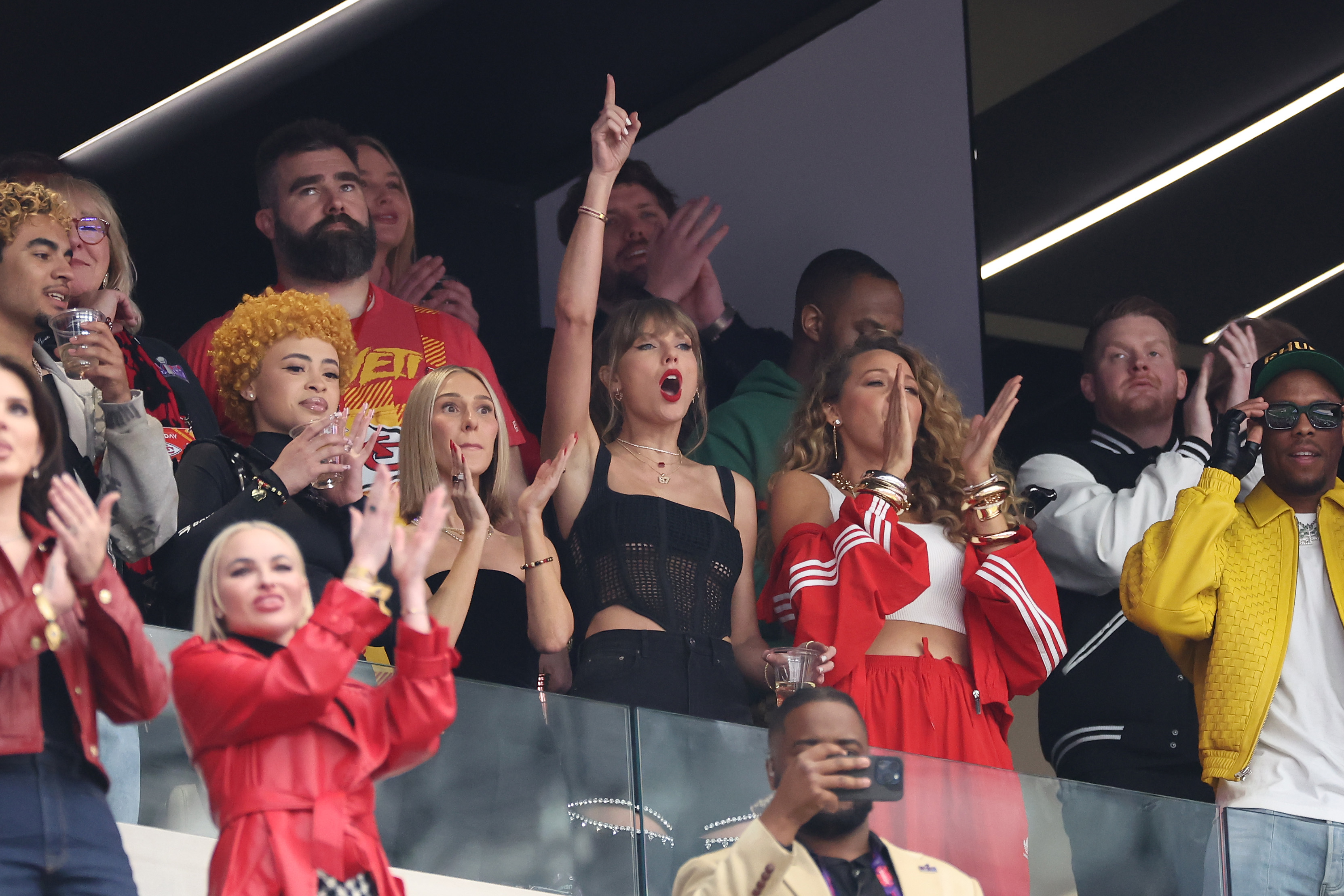 Taylor Swift passionately cheers alongside Brittany Mahomes and friends in a lively stadium box. Fans and other guests also celebrate around them