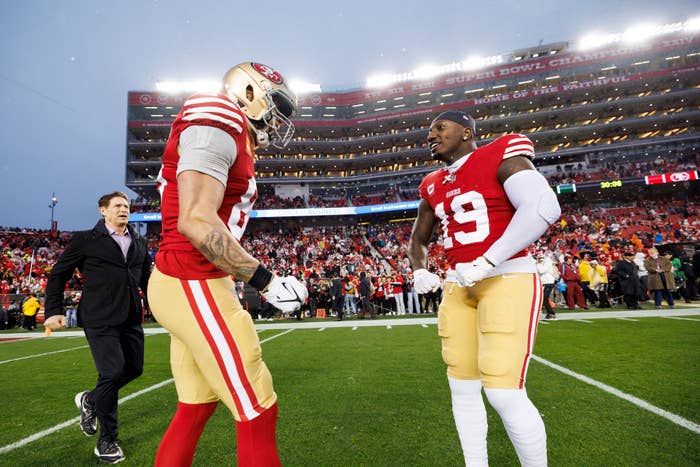 George Kittle and Deebo Samuel of the San Francisco 49ers on the field at Levi&#x27;s Stadium, with a man in a suit walking in the background