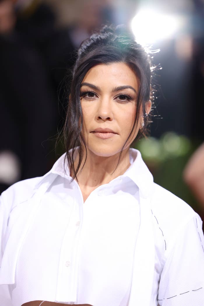 Kourtney Kardashian at an event, wearing a collared top with a subtle design, hair styled in an elegant updo