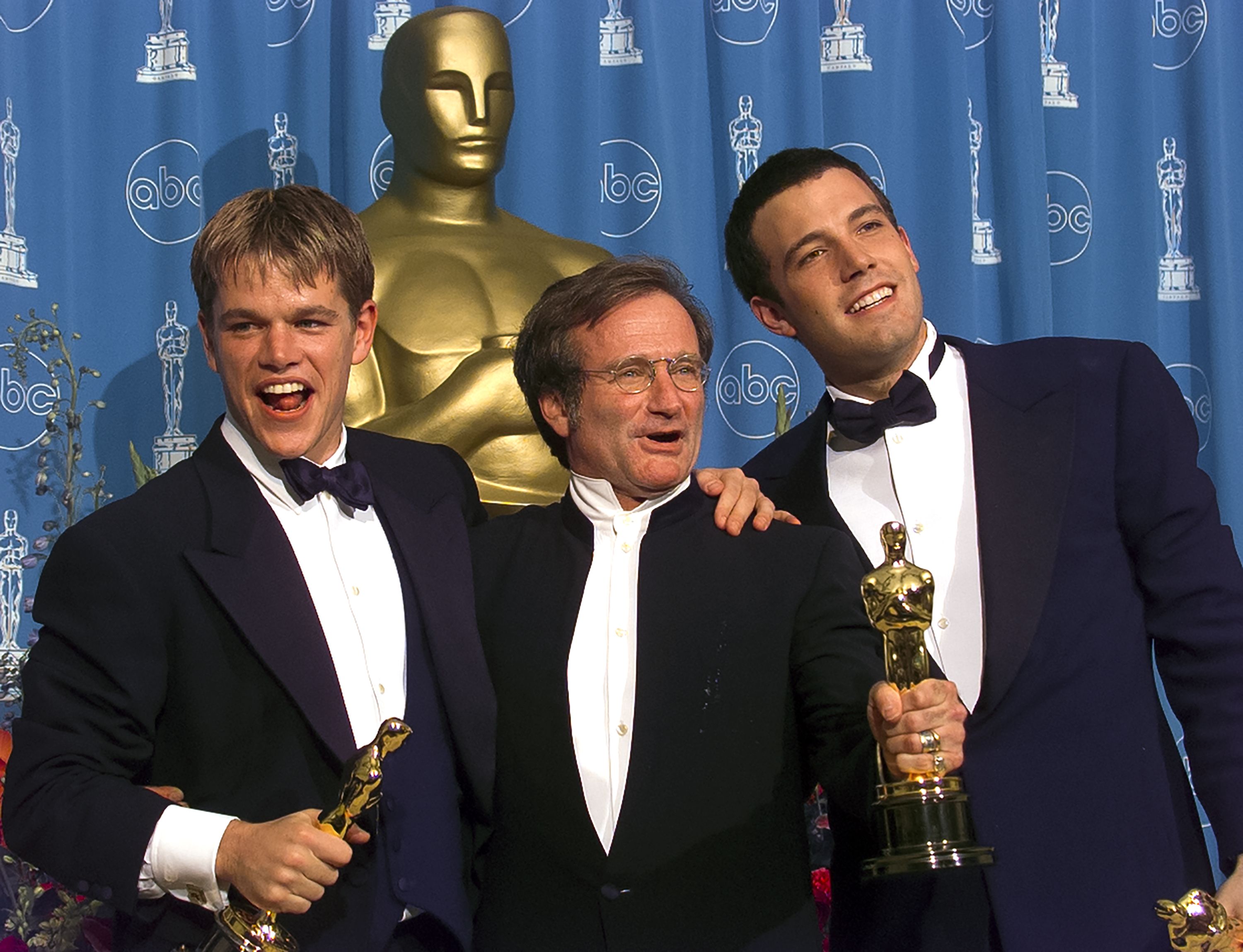 Matt Damon, Robin Williams, and Ben Affleck at an awards event, each holding Oscars, smiling in front of a backdrop with an Oscar statuette and ABC logos