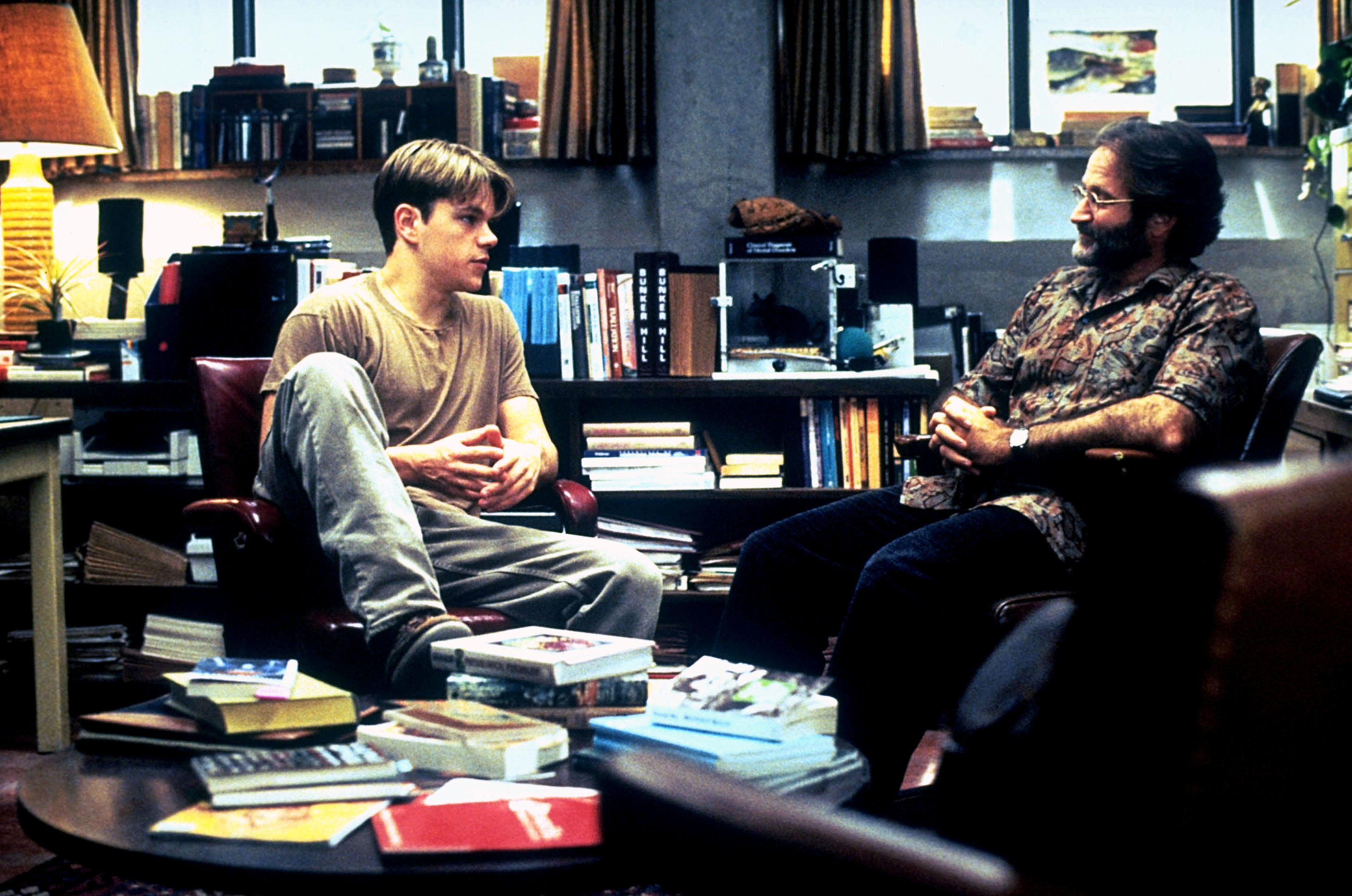 Matt Damon and Robin Williams sit in a cozy, book-filled office, engaged in conversation