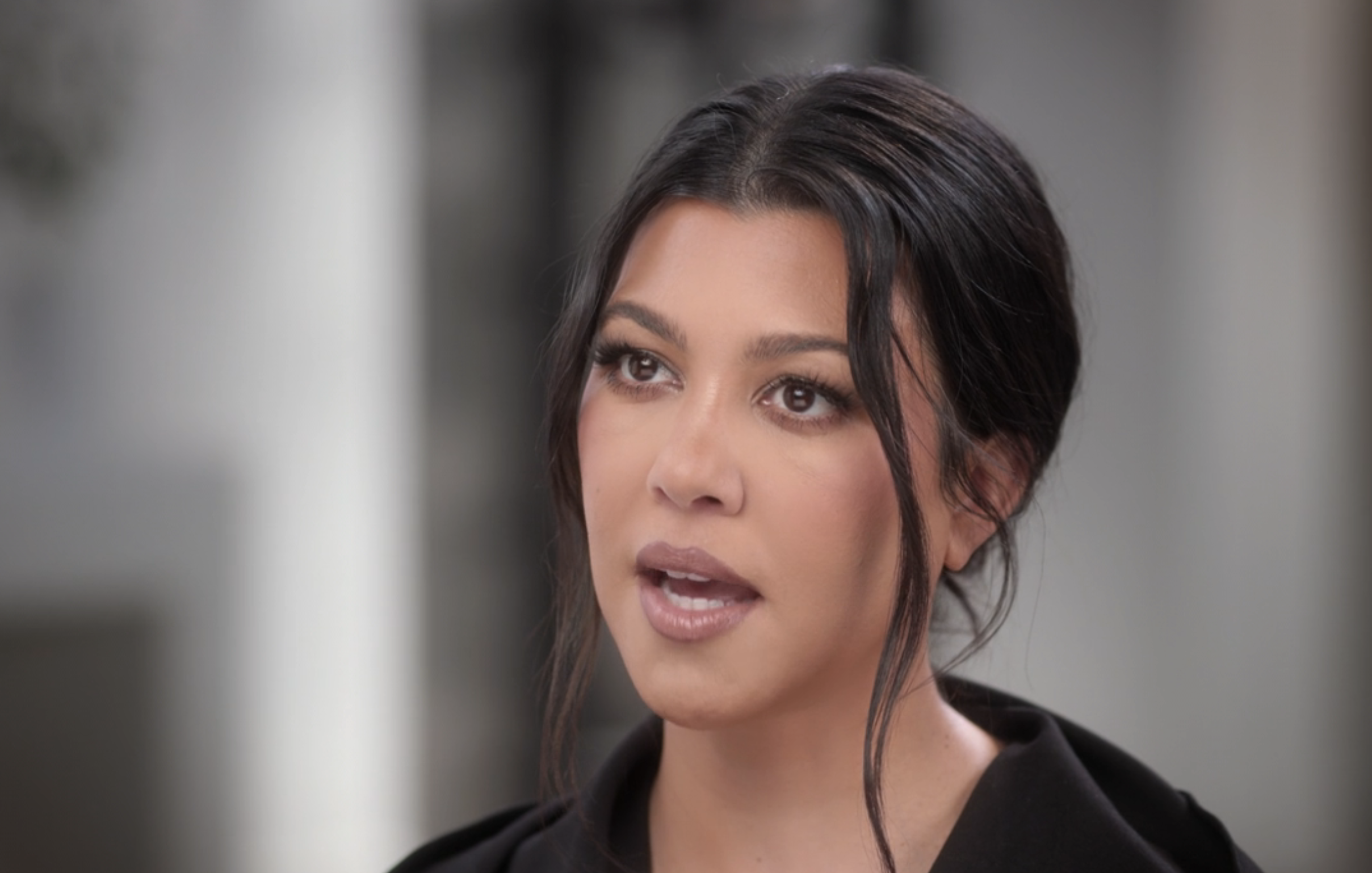 Kourtney Kardashian speaking in an interview setting, with a neutral expression and styled hair