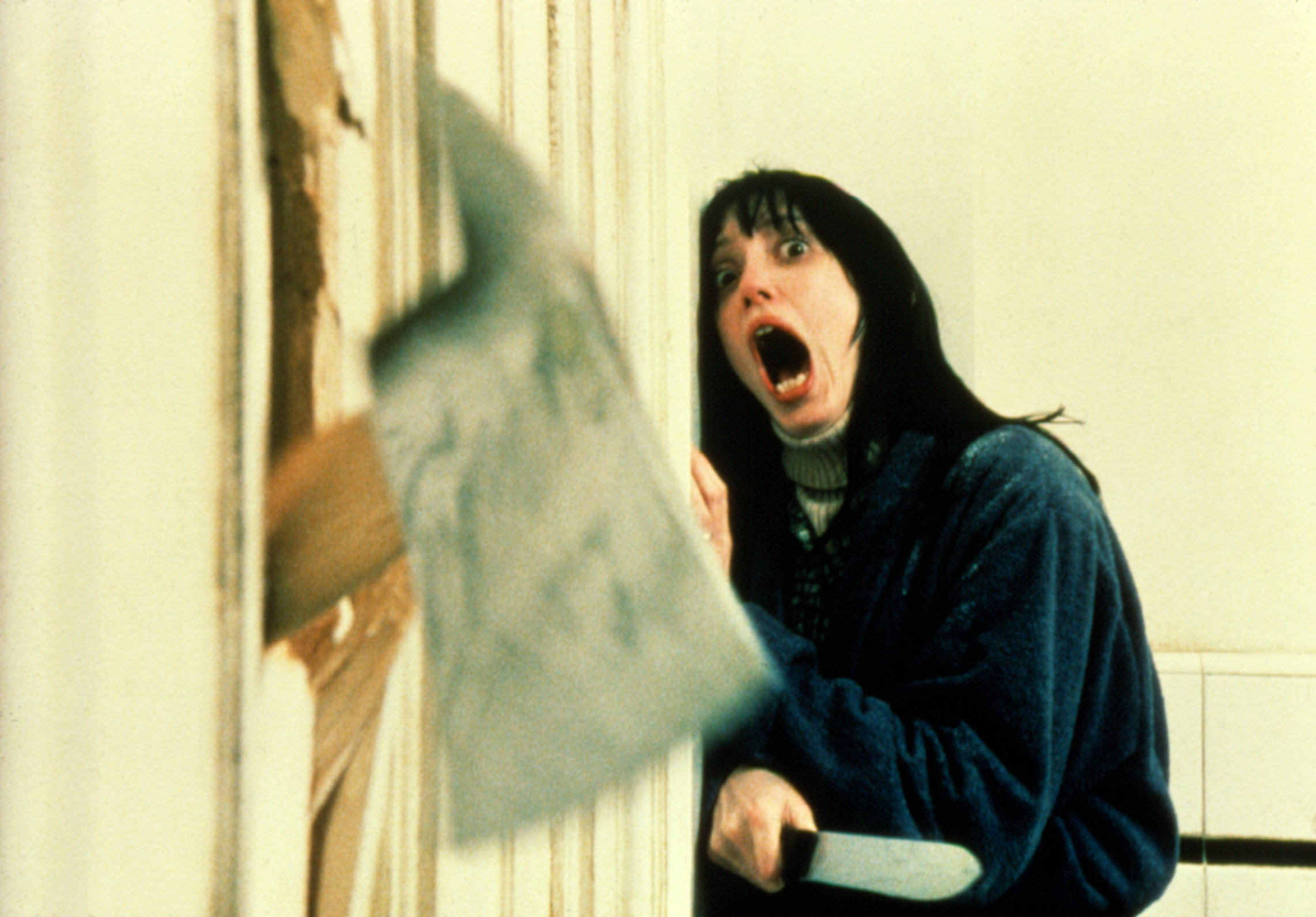 Shelley Duvall in a memorable scene from the film &quot;The Shining,&quot; screaming while holding a knife as an axe breaks through a door