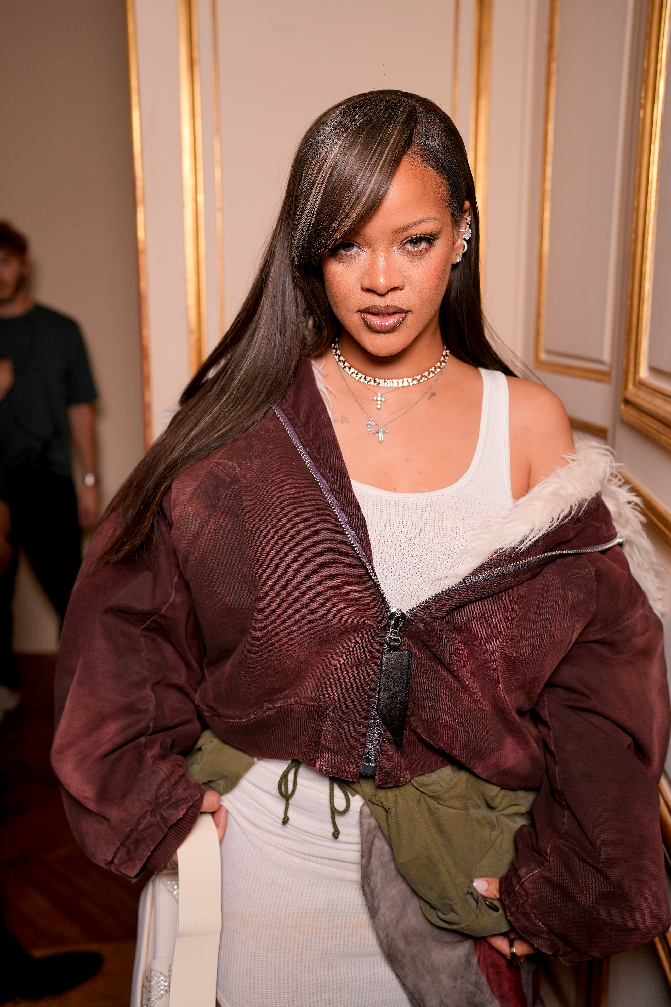 Rihanna at an event, wearing a stylish white dress paired with a burgundy jacket and multiple necklaces