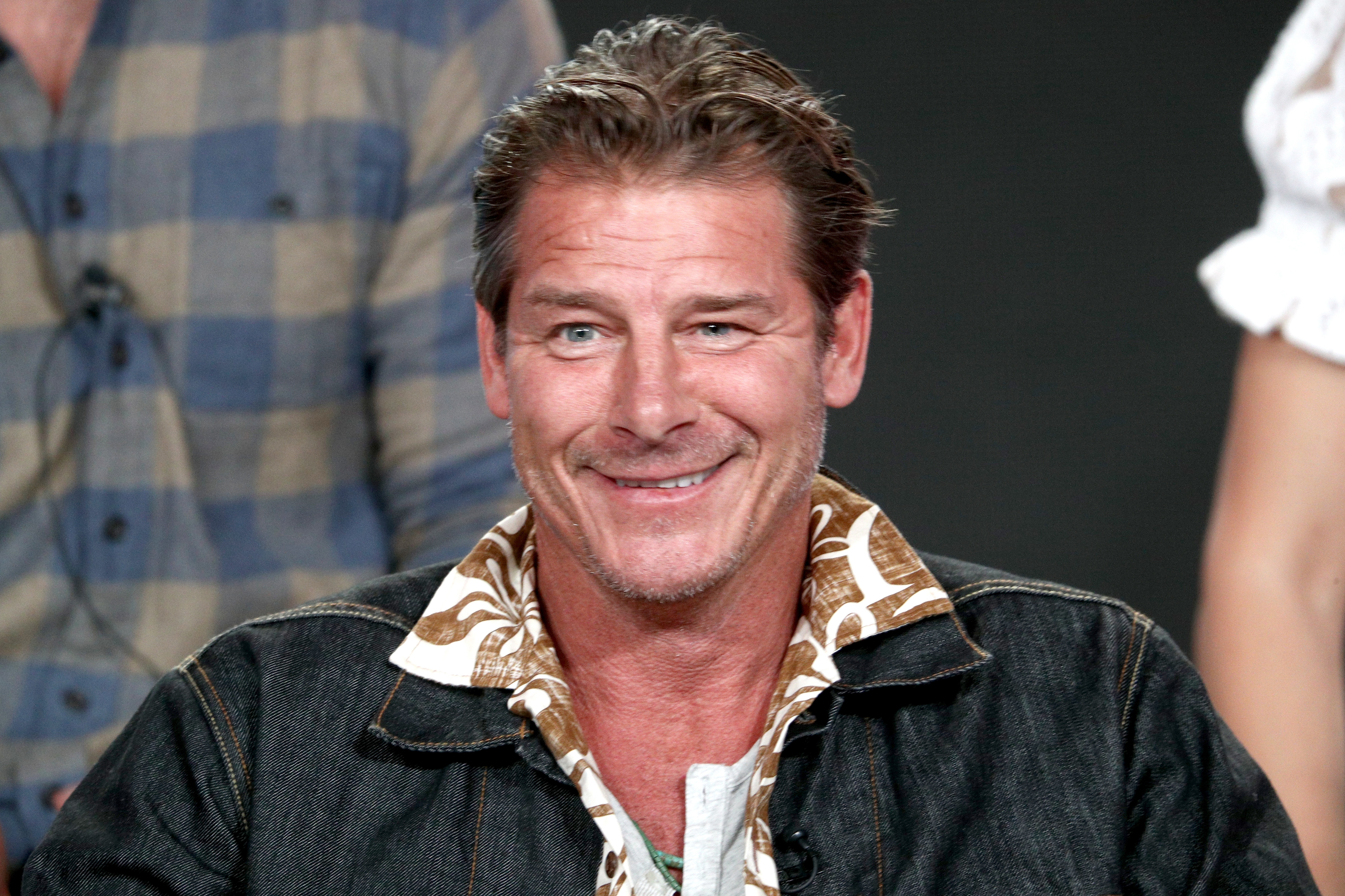 A smiling man dressed in a patterned shirt and a denim jacket